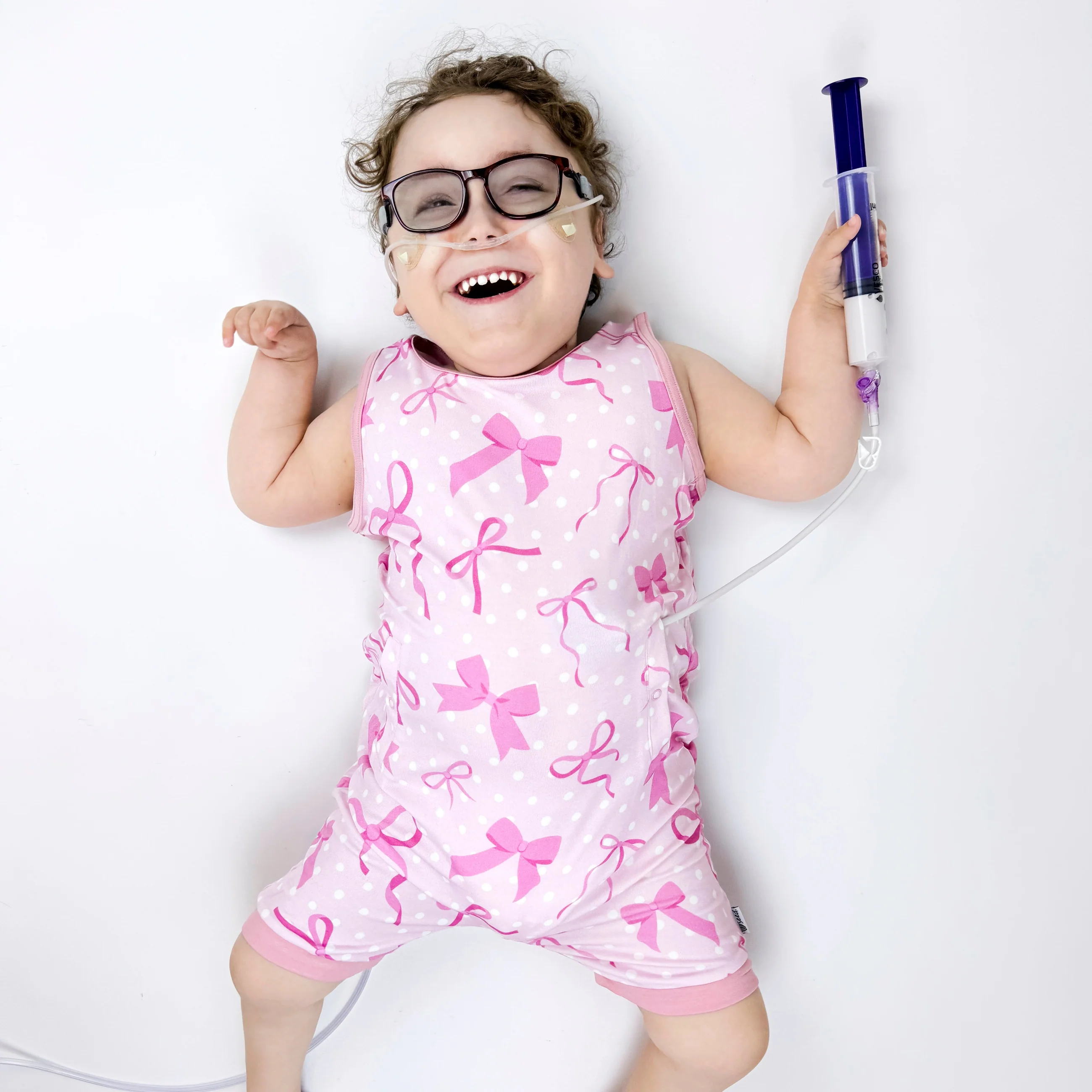 Girl wears pink bow patterned romper with feeding tube in her hand
